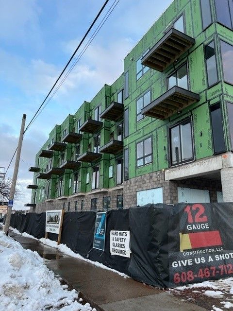 Multi-story building under construction with green wrap, balconies, and black fencing.