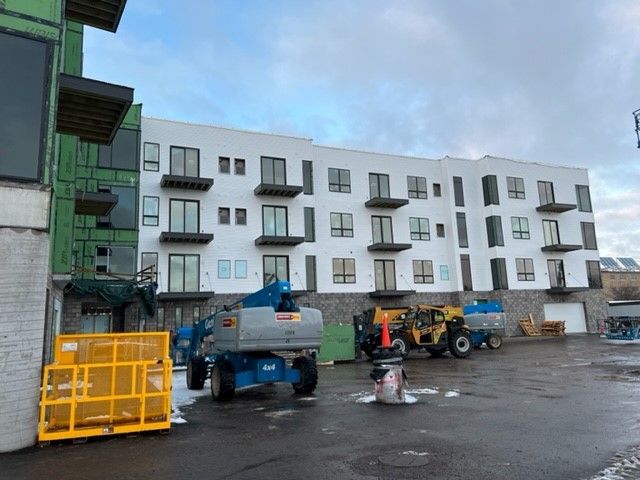 Construction site: white apartment building, blue lift, construction vehicles, cloudy sky.