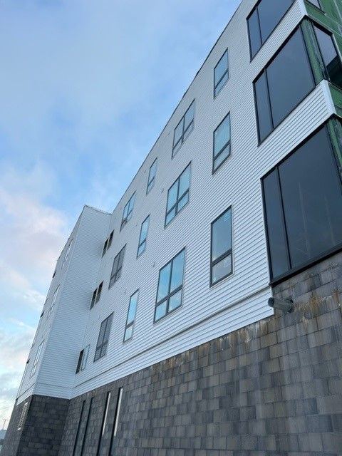 Multi-story building with white siding and gray brick base against a cloudy sky.