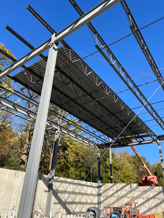 Steel framework of a building under construction, with dark roof panels and a blue sky in the background.