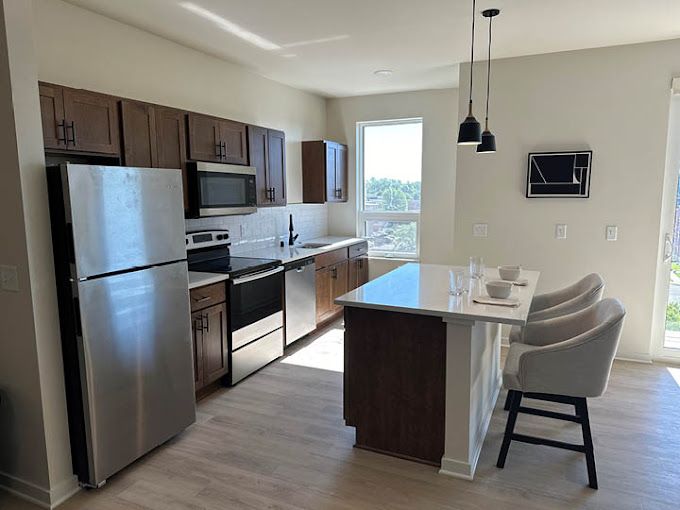 Modern kitchen with stainless steel appliances, dark cabinets, a white island, and light wood flooring.