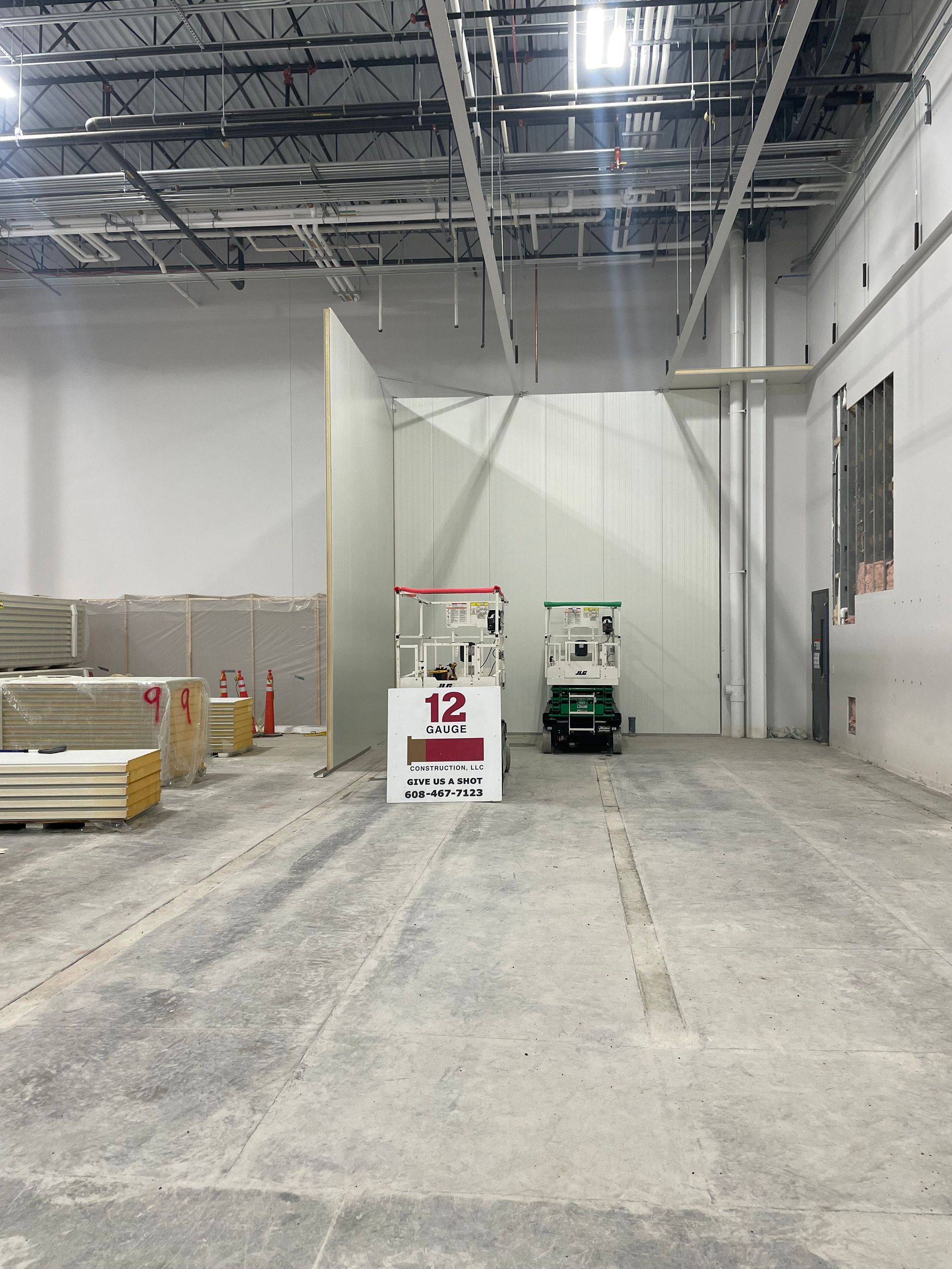 Construction site interior with concrete floor, white walls, lift equipment, and building materials.