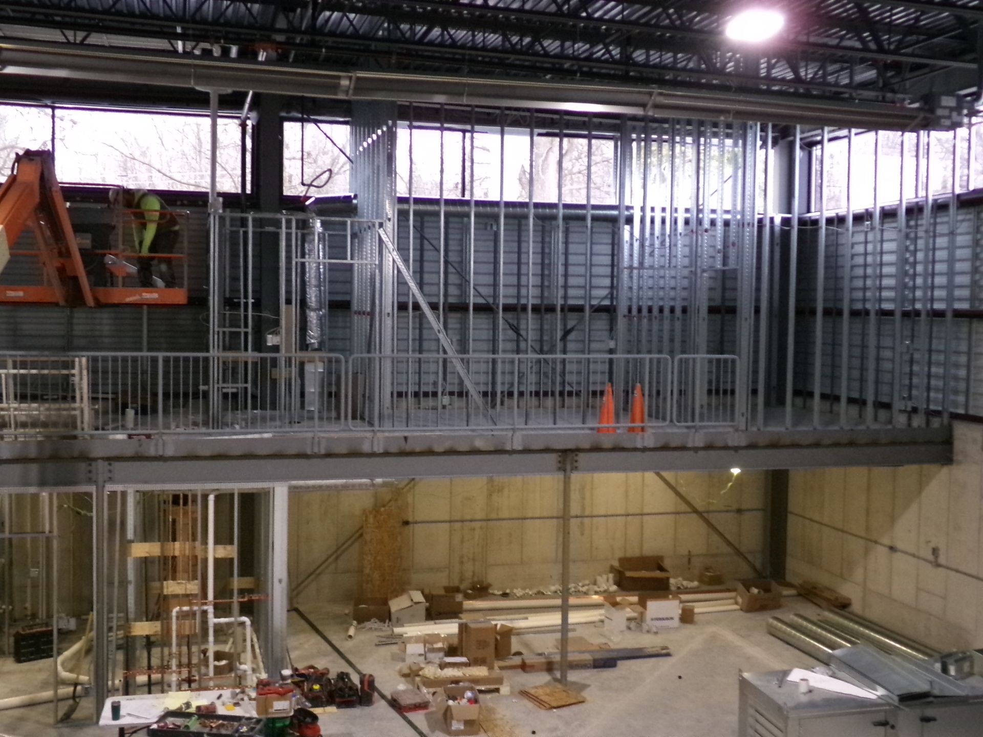 Construction of a two-story building interior with metal framing, including a worker in a lift.