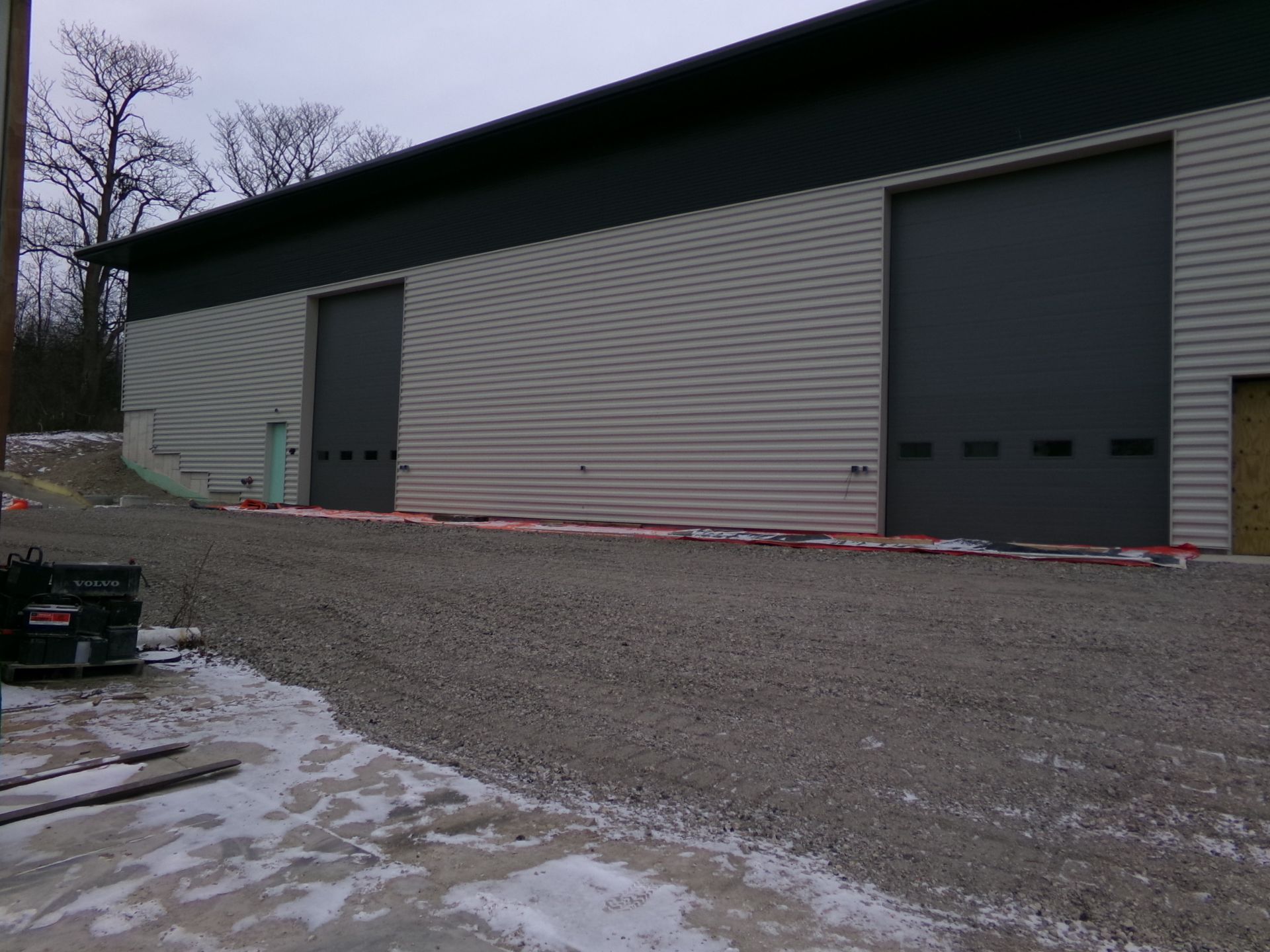 Building with two large gray garage doors on a gravel drive, with patches of snow.
