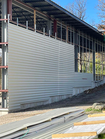 Construction site, metal siding being installed on building with exposed steel beams and concrete foundation.