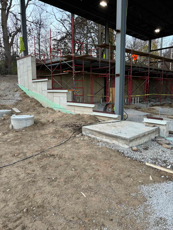 Construction site with concrete steps, retaining wall, scaffolding, and a partially built structure under a metal roof.