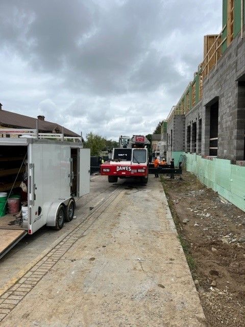 Construction site with a red forklift, trailer, and building under construction. Cloudy sky.