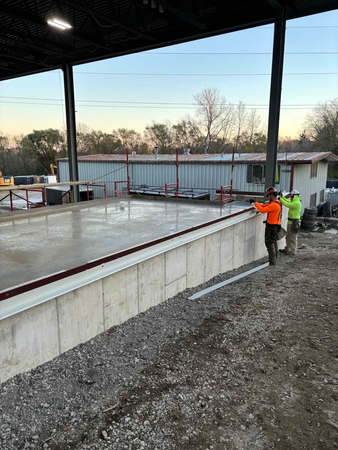Two construction workers on a new concrete structure with a building and sky in the background.