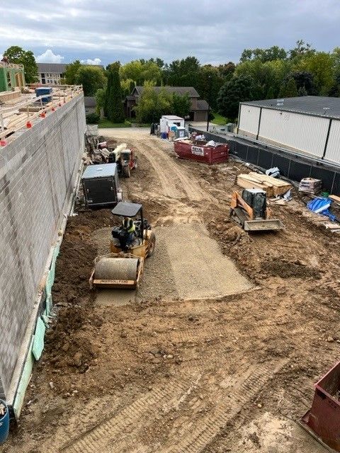 Construction site with a soil compactor, excavator, and red dumpster.