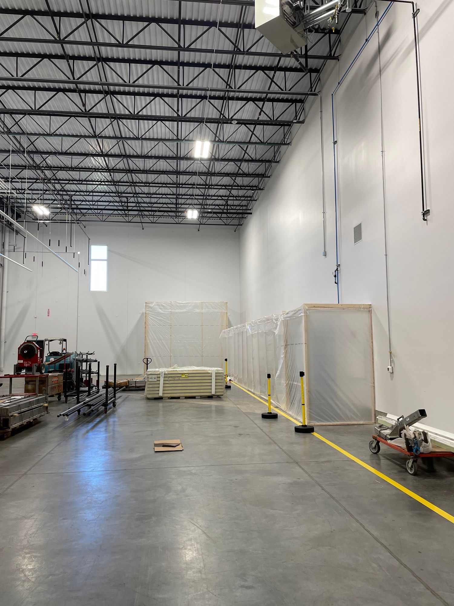 Empty warehouse interior with high ceilings, concrete floor, and equipment.