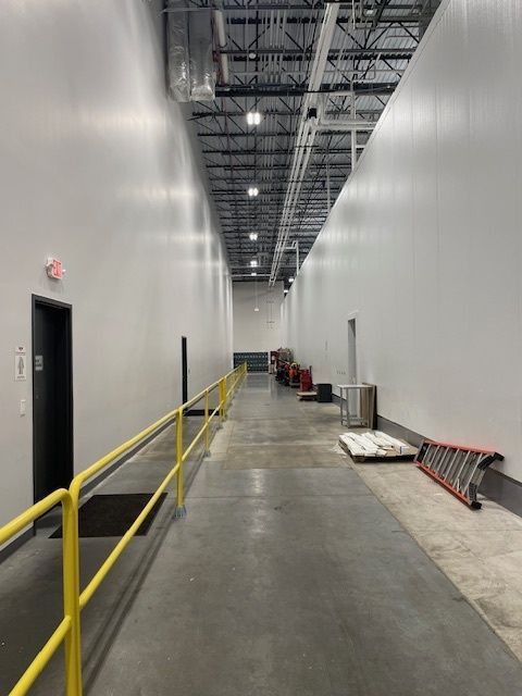 Long, narrow warehouse hallway with white walls, a gray floor, and a yellow safety rail.