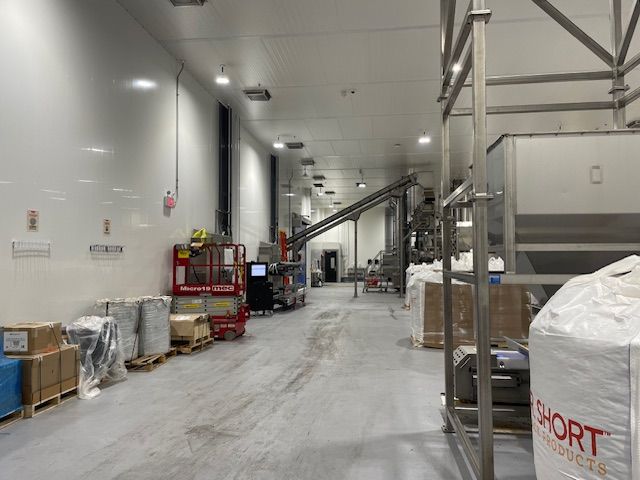 Inside a food processing plant: A long hallway with processing equipment, pallets, and bags.