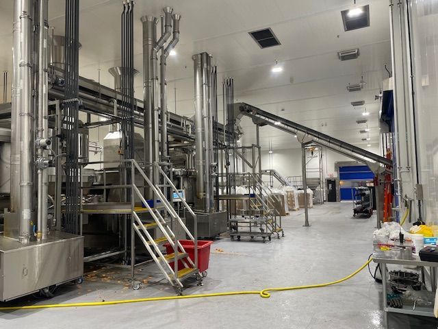 Factory interior with stainless steel machinery, pipes, and a conveyor belt.