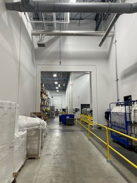 Warehouse interior with loading dock and forklift. White walls, gray floor, yellow railing.