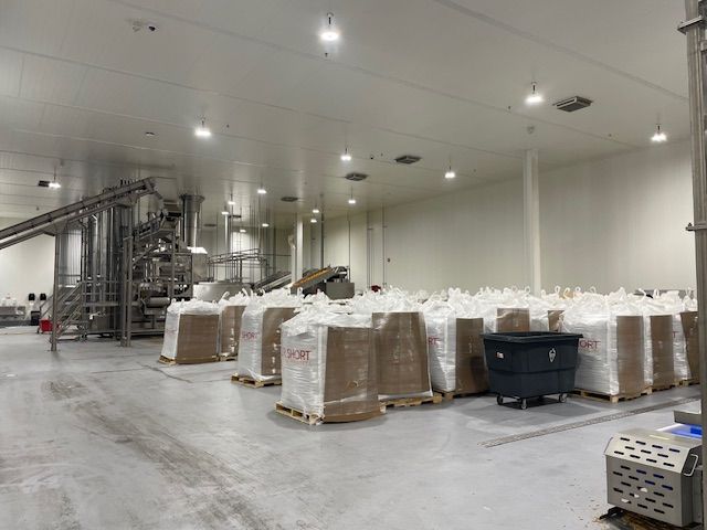 Large warehouse with pallets of wrapped goods and industrial machinery.