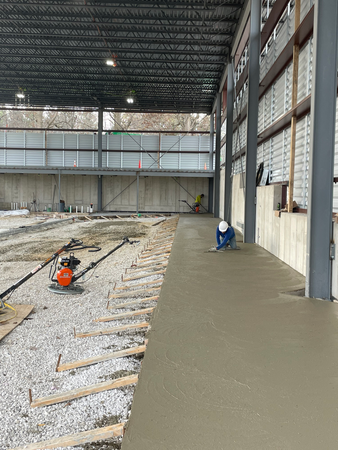 Construction workers pouring concrete in a large building. One worker is smoothing the wet concrete.