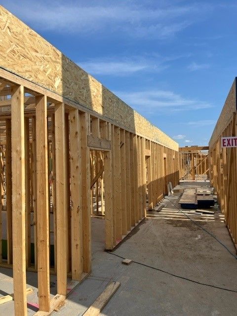 Wooden framework of a building under construction on a sunny day. Interior hallway visible with an 