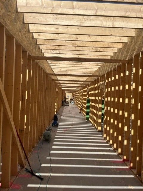 Wooden framework of a long hallway under construction; sun casts shadows through the beams.