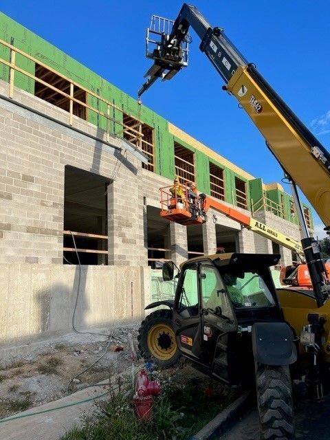 Construction site with a telehandler lifting material; workers on a lift, building exterior with block and wood framing.