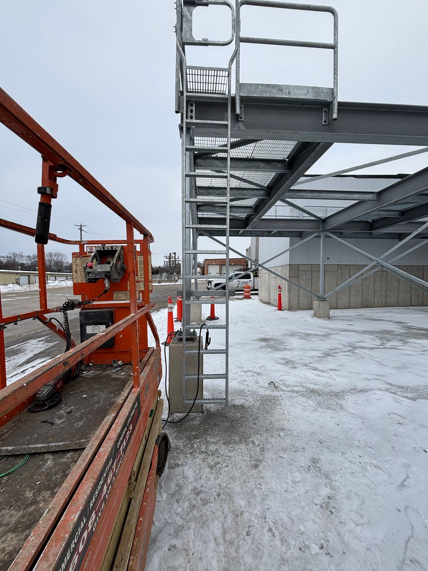 Construction site with a scissor lift, metal ladder, and partially built building. Snowy ground.