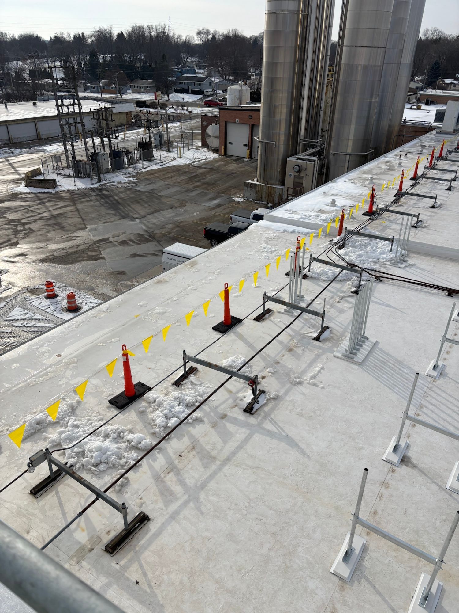 Rooftop edge with safety railing and yellow flags. Cement silos and snow-covered ground visible in background.