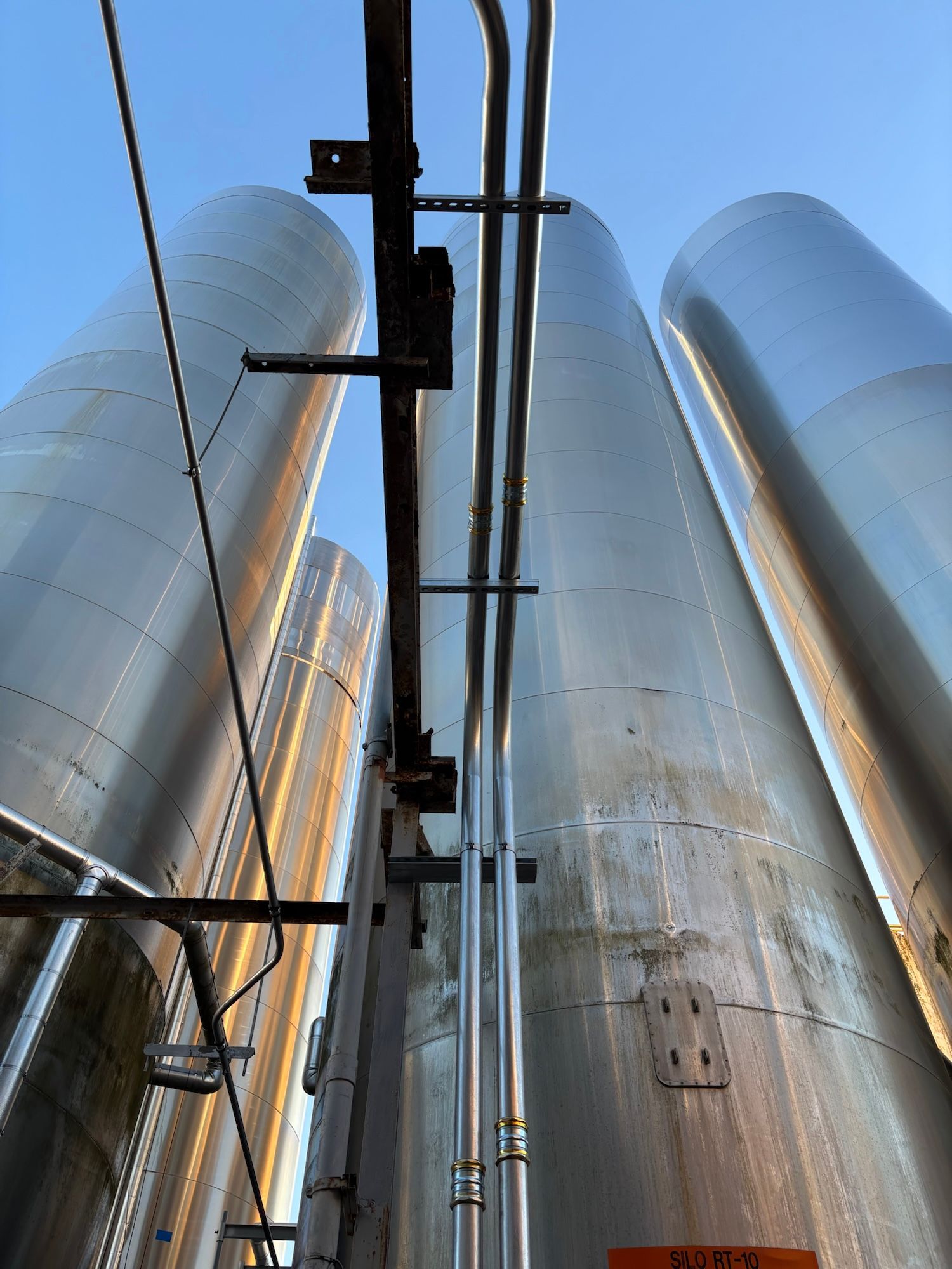 Vertical cylindrical metal storage tanks against a blue sky, with pipes and support structures visible.