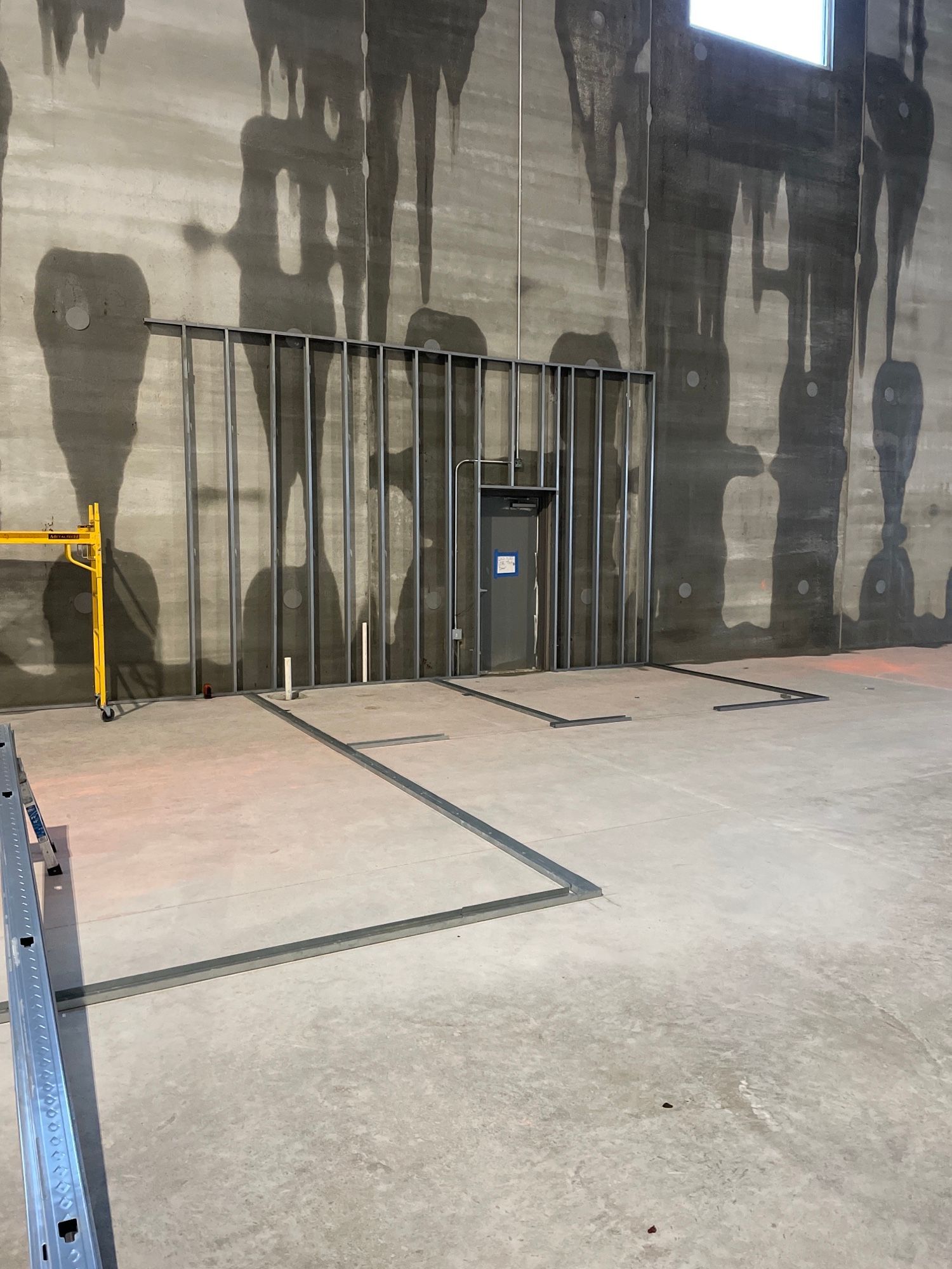 Industrial concrete room with a metal door, exposed pipes, and dark water stains on the walls.