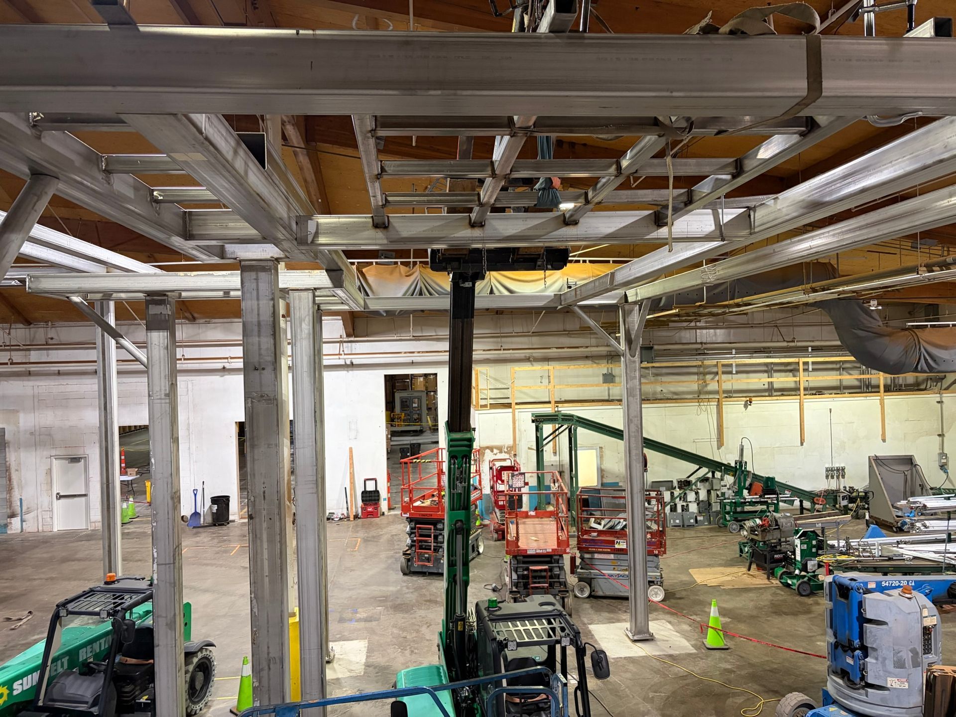 Large industrial workshop with exposed ceiling beams, columns, and construction equipment scattered around.