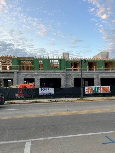 Construction site with building frame, green scaffolding, black fencing, banners, street, and sky.