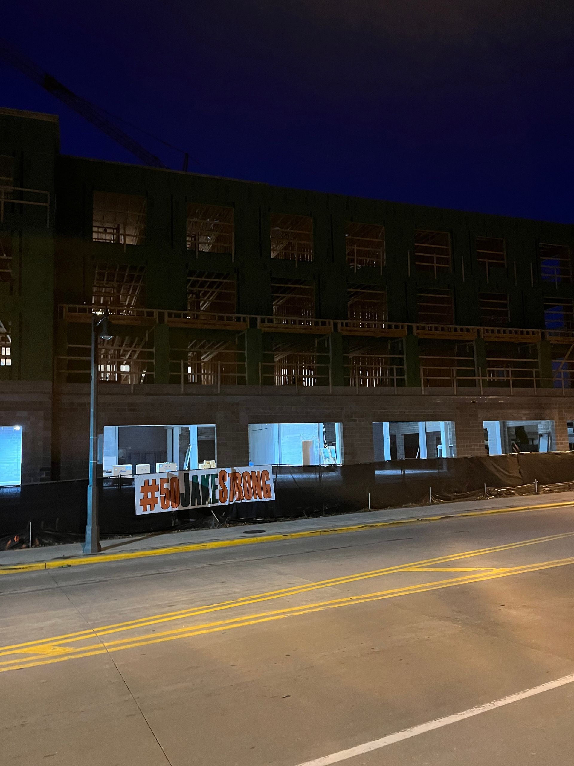 Large brick building at dusk with construction scaffolding, lit windows, and a banner reading 