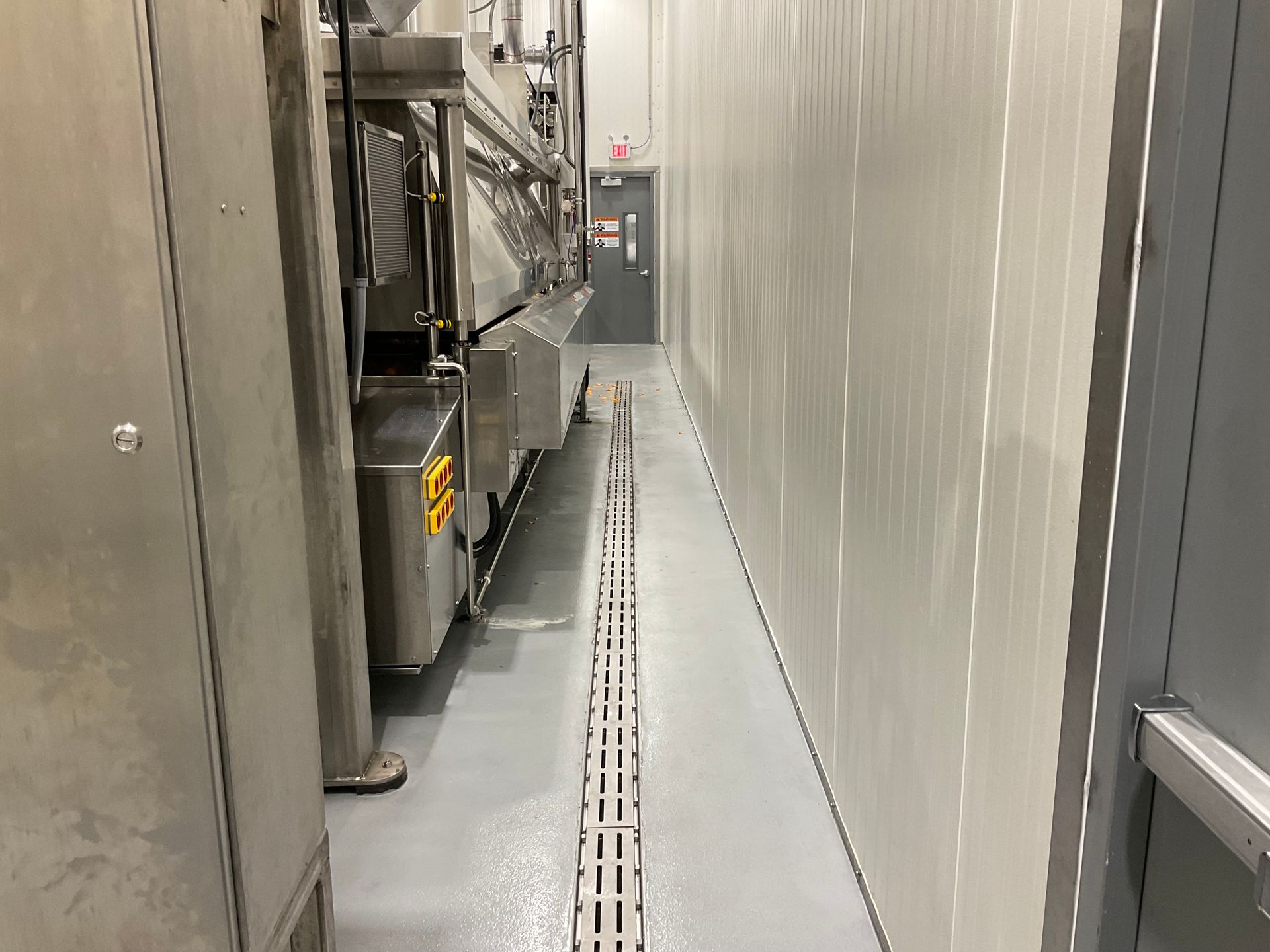 Narrow industrial hallway with stainless steel equipment and a drain in the floor.