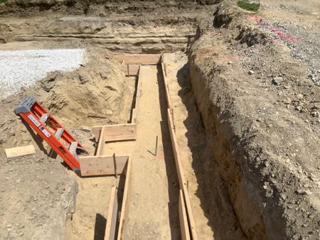 Foundation construction site with wooden forms, dirt trenches, and a ladder.