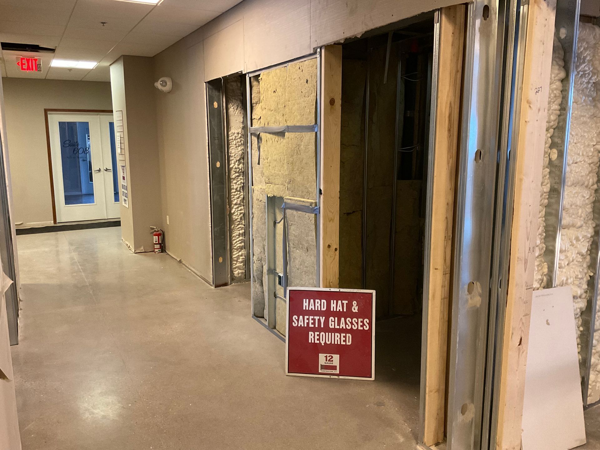 Hallway under construction; exposed wall studs, insulation, and warning sign.
