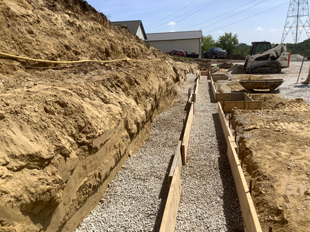 Construction site with trench filled with gravel, wooden forms for foundation work.