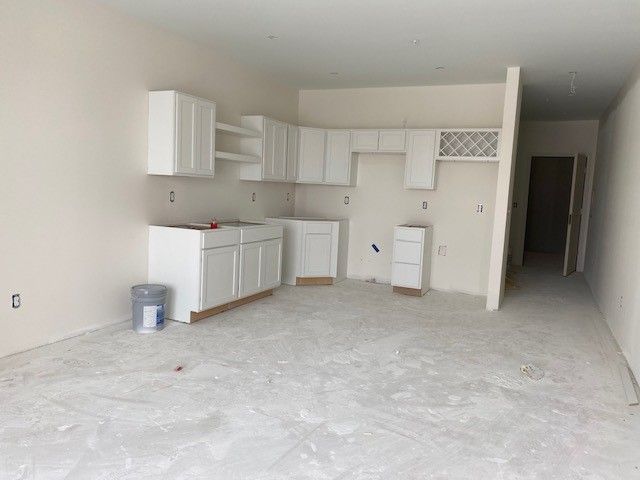 Interior view of a kitchen under construction with white cabinets, light walls, and concrete flooring.