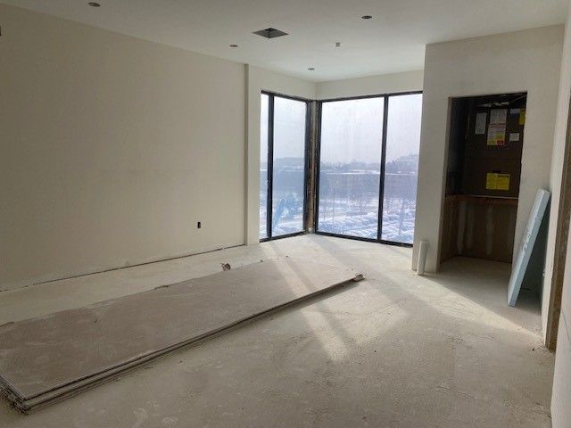 An unfinished room with large windows, drywall, and a doorway.