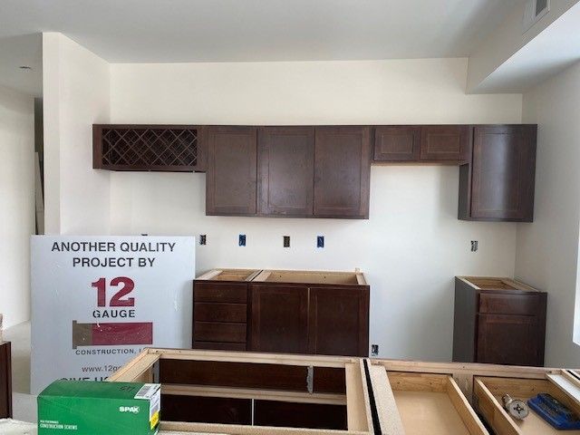 Kitchen under construction with brown cabinets, white walls, and a wine rack.