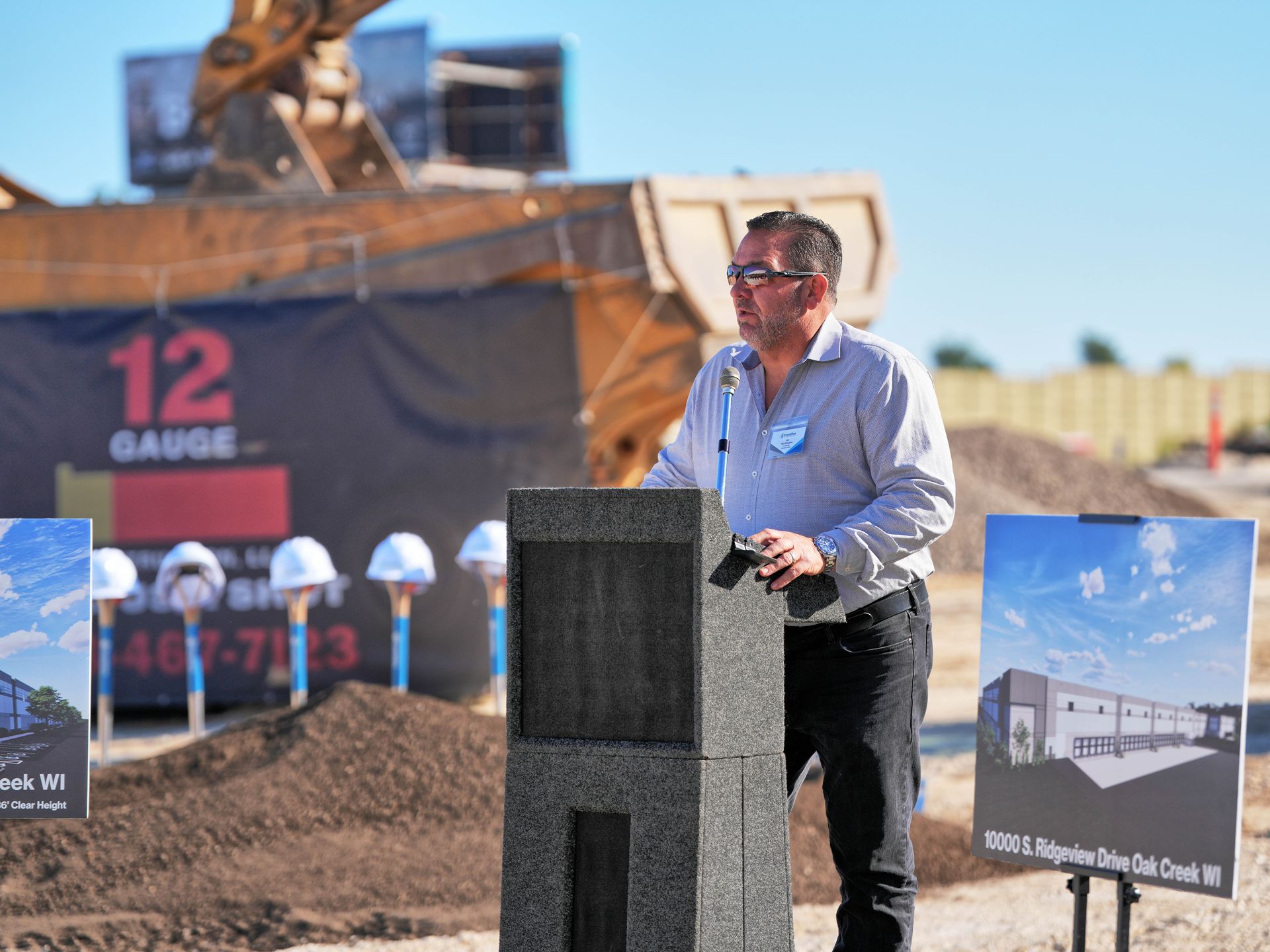 Man speaking at a podium at a construction site; 