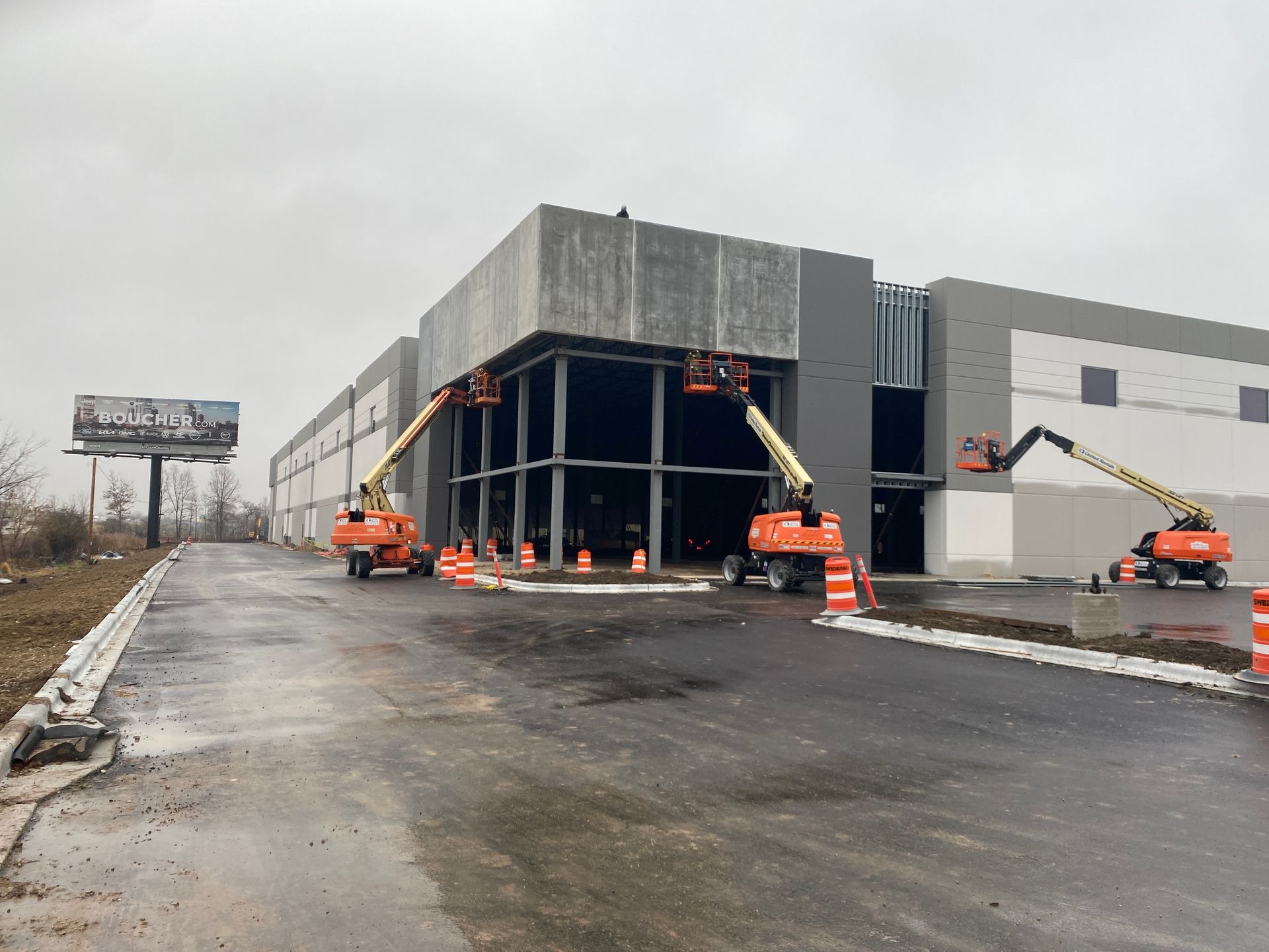 Construction site: workers on lift equipment installing panels on a large building with dark gray and white walls.
