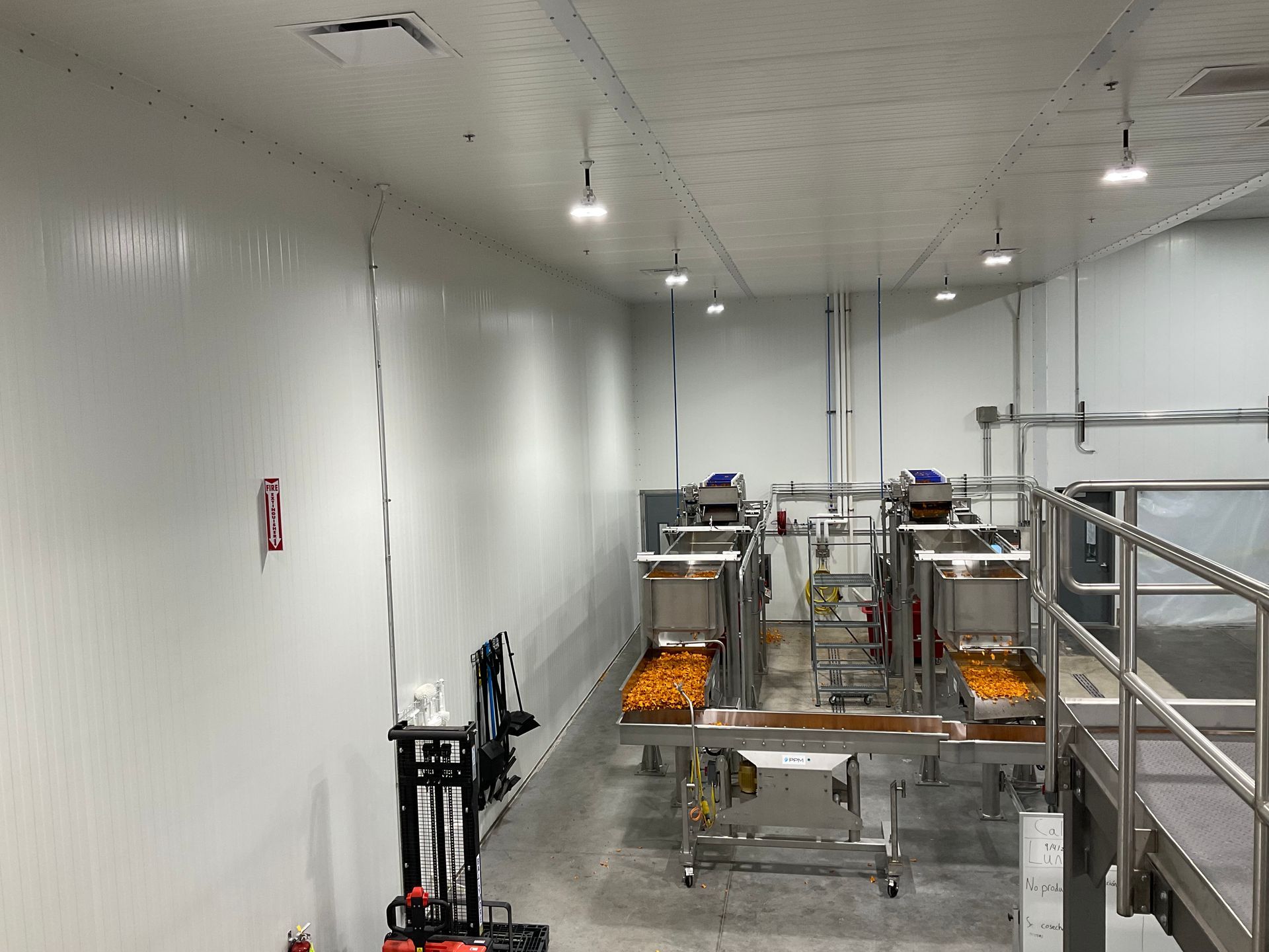White-walled food processing facility. Conveyor belts and machinery are visible. Fluorescent lights and a service panel.