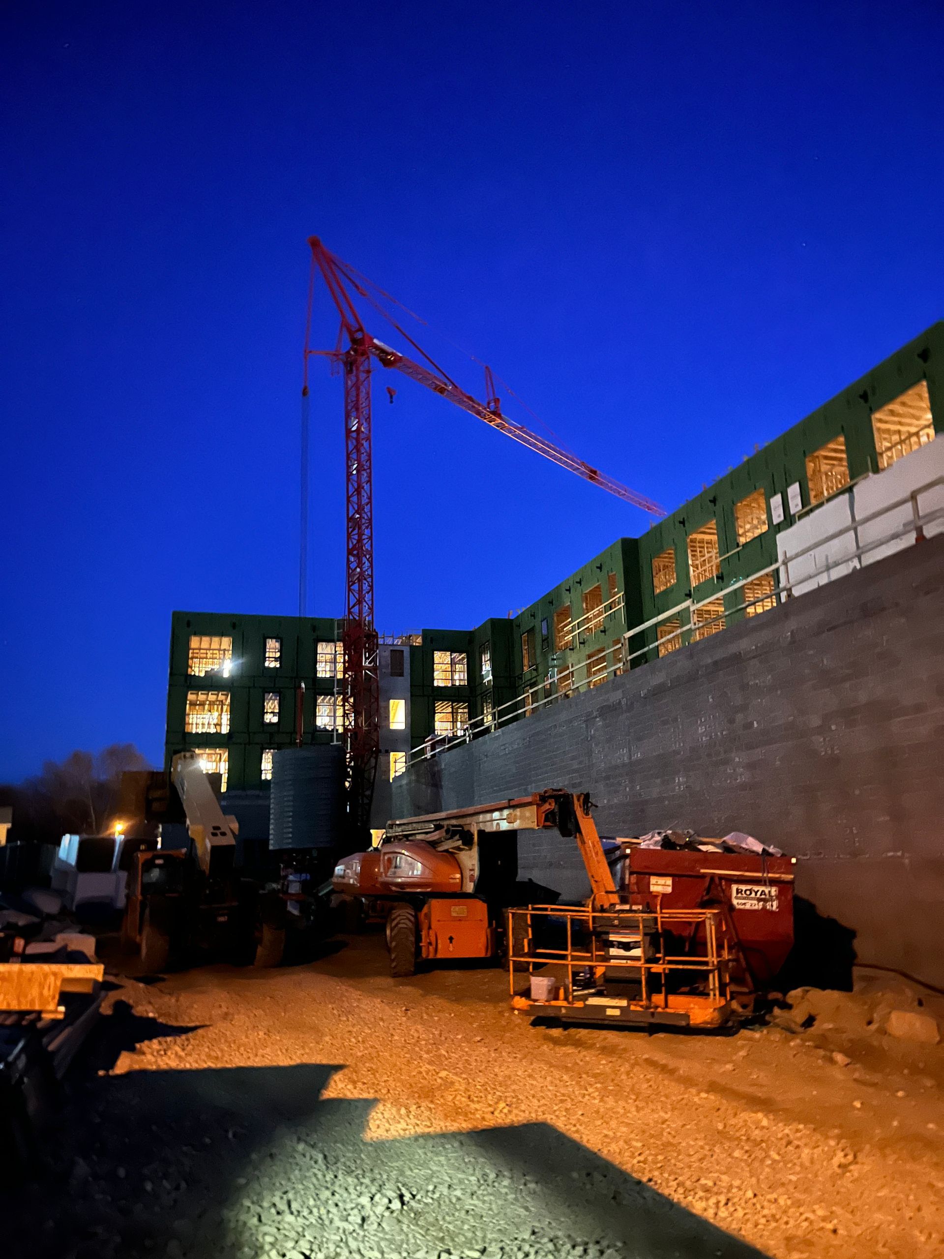 Construction site at night with cranes, building, and equipment against a dark blue sky.