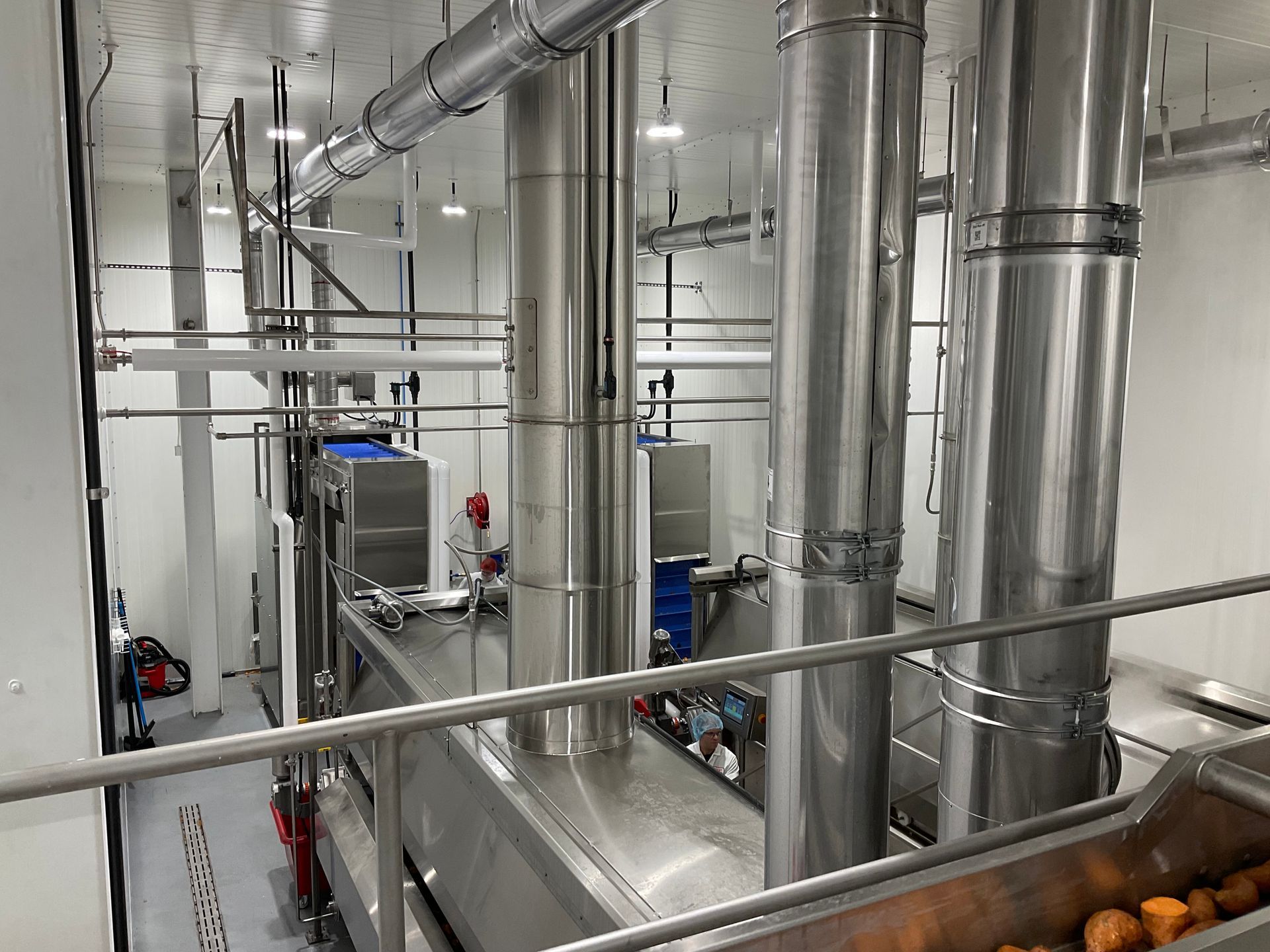 Stainless steel food processing equipment in a clean, industrial setting with pipes and machinery.