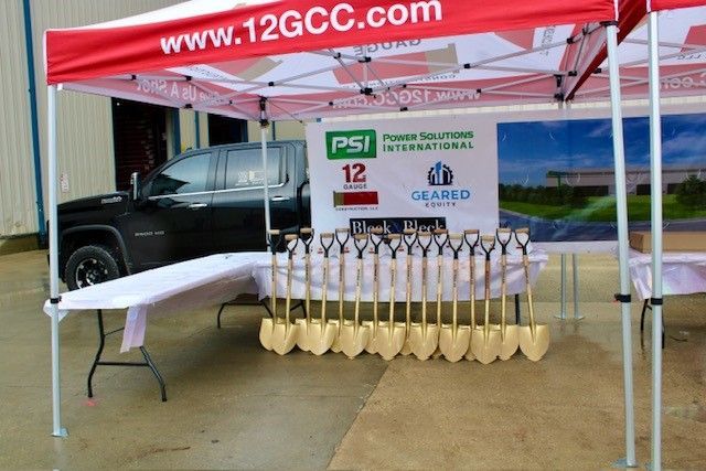 Groundbreaking ceremony with gold shovels, tent, truck, banner.
