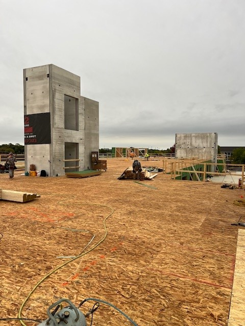 Construction site with concrete structures against a cloudy sky. Wooden planks and tools are visible.