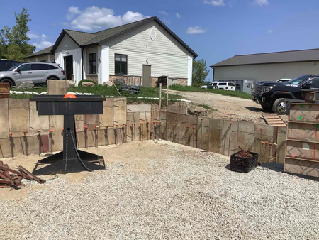 Construction site with retaining walls, gravel, and a black grill in front of a house.