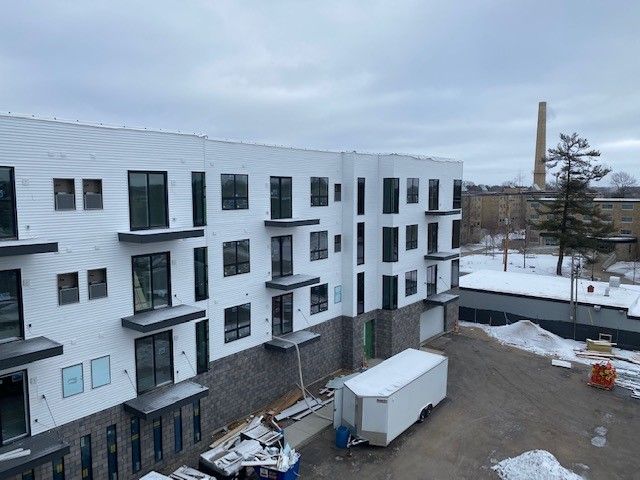 Exterior of a modern apartment building under construction on a snowy day. White siding, black trim, and a smokestack.