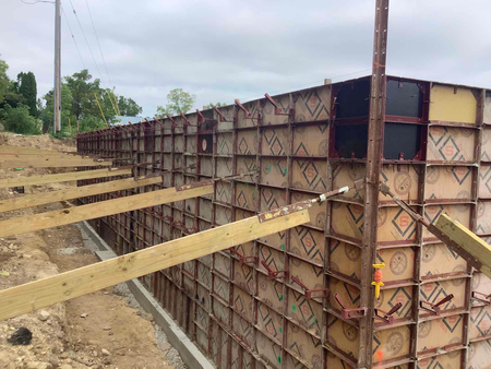 Formwork for a concrete retaining wall under construction, with wooden supports and panels.