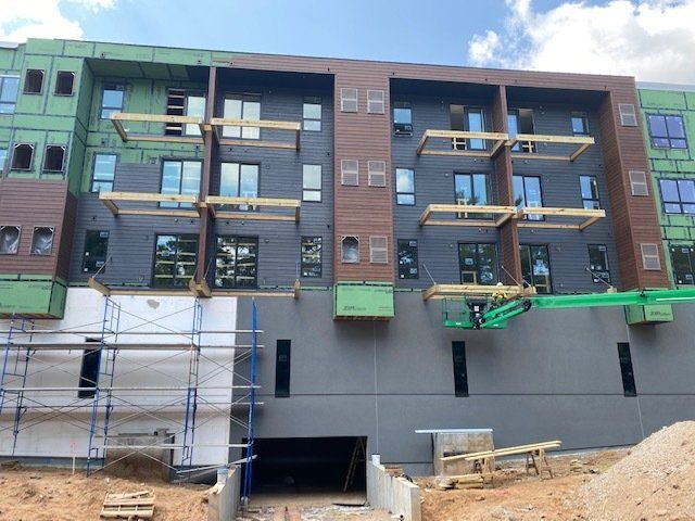 Apartment building under construction; gray and brown exterior with scaffolding and lift.