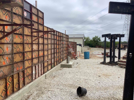 Construction site with concrete formwork, gravel ground, blue barrel, and a cloudy sky.