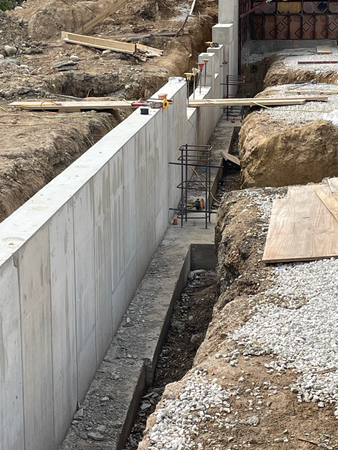 Concrete foundation wall under construction, trench, rebar, construction site.